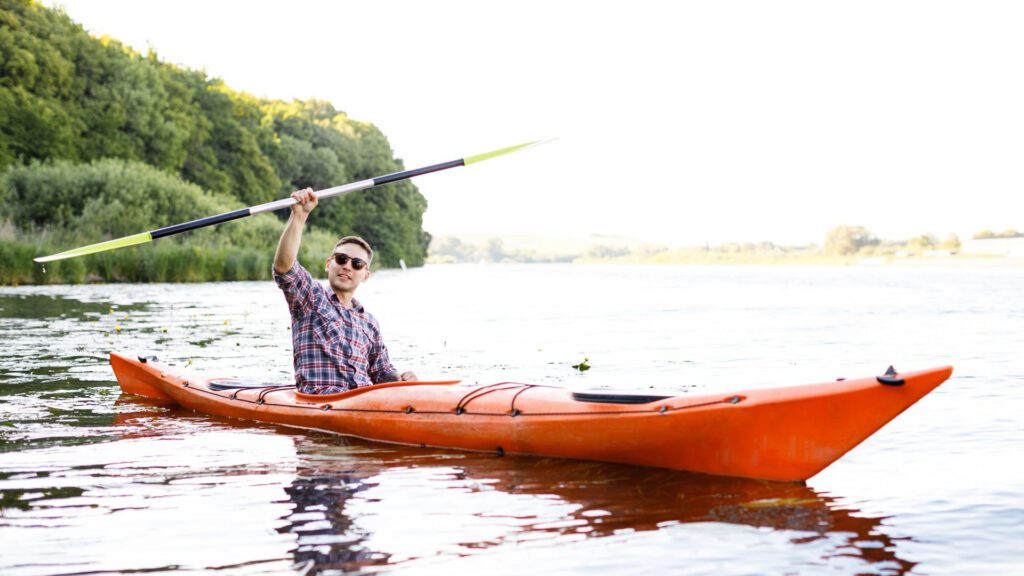 Man in orange kayak holding paddle on calm water,